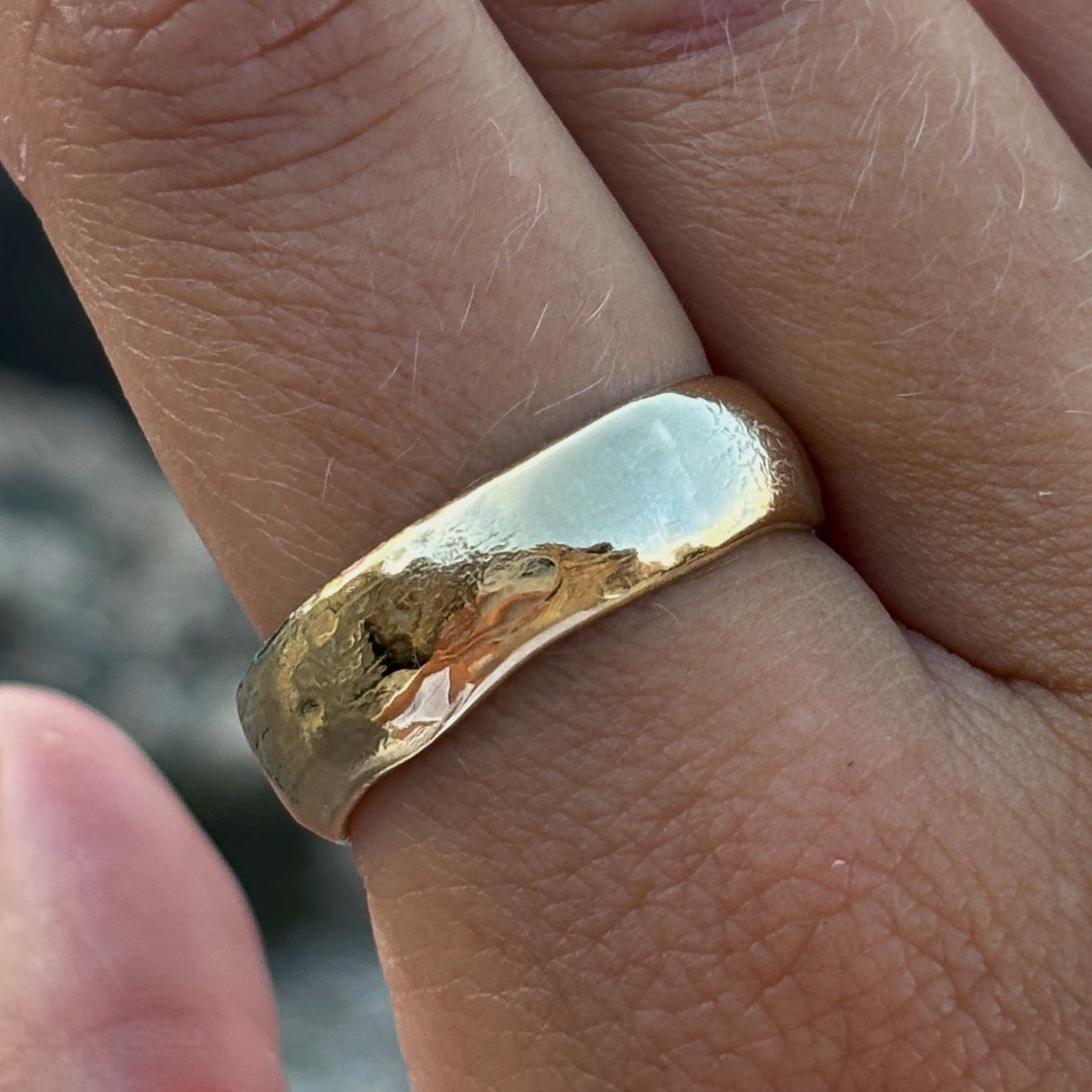 Hand wearing two gold rings with a blurred natural background