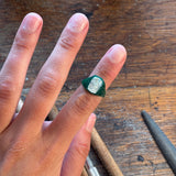 Hand wearing a green gemstone ring on a wooden surface with tools.