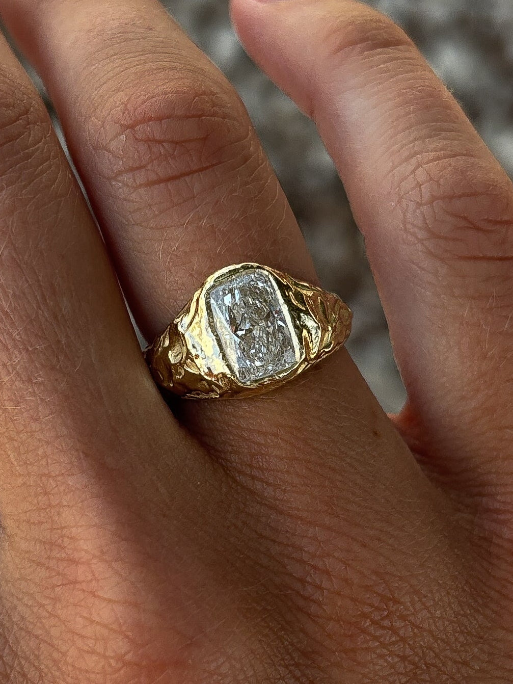 Hand wearing a gold ring with a large diamond on a blurred background