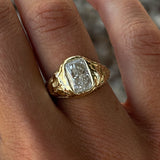 Hand wearing a gold ring with a large diamond on a blurred background
